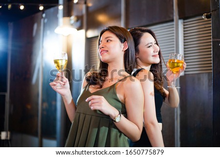 two Asian young woman holding glasses of wine toasting and celebrating on rooftop party together with cheerful drink dance with party music, happy girl smile for fun night club, hang out with friend  
