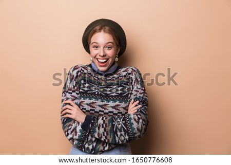 Photo of pretty excited woman in earrings smiling and posing hands crossed isolated over beige background