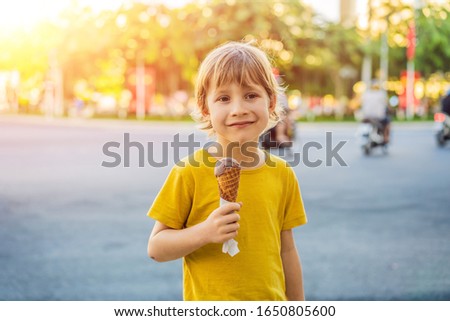 Cute little boy, eating big ice cream in the park, smiling at camera, summertime