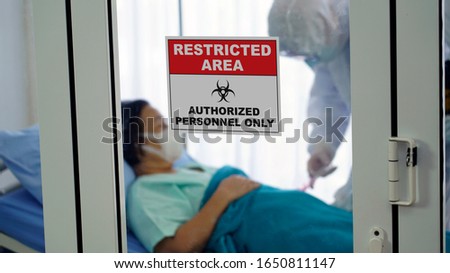 Restricted area : Authorised personnel area signage in front of control room with infected female patient and doctor in protective suit inside. Coronavirus Covid 19 Quarantine area.