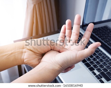 young asian woman suffering with hand pain from working with laptop computer, aches and pain medical concept.