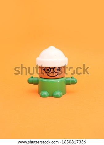 Mini cute cartoon figure toy with white hat and green clothes on orange background