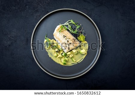 Gourmet fried cod fish filet with caviar, avocado slices and mustard mango creme as top view on a modern design plate with copy space 