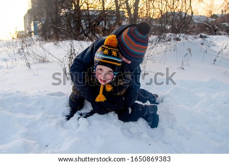 Two little European boys play and fight in the snow in winter.
