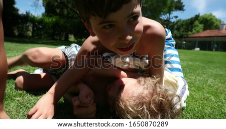 
Brother wrestling younger toddler outside in backyard home. Siblings quarrel conflict outdoors