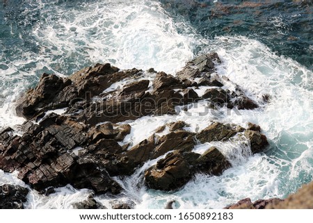 Scenic of large rouge stones at shoreline with strong wavy sea water, viewing from top as natural seaside outdoor background theme.