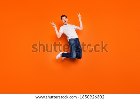 Full size photo of positive cheerful guy jump enjoy spring free time holidays make v-sign wear casual style stylish outfit gumshoes isolated over bright color background