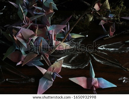 These orizurus (paper cranes, origami birds) broke the glass jar and escaped, settled down on the branches. Close up picture of unicorn colored Japanese origami birds in front of black background.