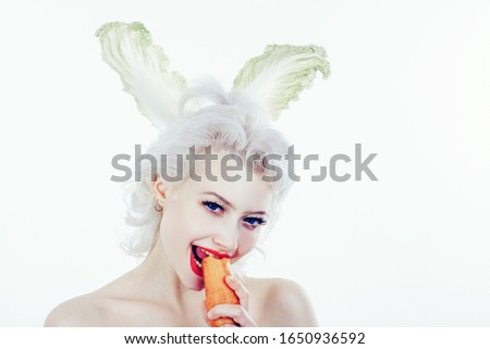 Beautiful young girl with bunny ears is eating carrot on color background.Copy space. Easter holiday