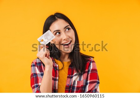 Photo of pleased brunette woman smiling while holding credit card isolated over yellow background