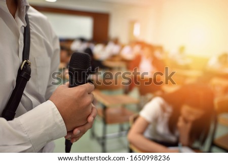Hand holding microphone in classroom for public speaking activity or for explaining subject assignment for the students to do/ public speaking or talking concept picture related to socializing work