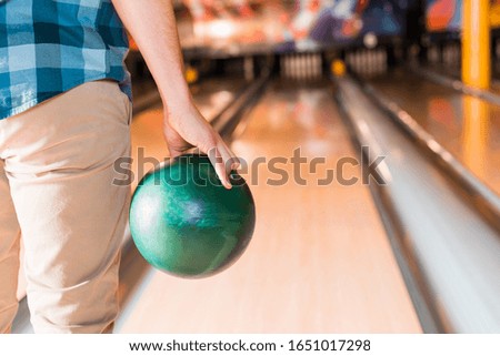 partial view of young man holding bowling ball near skittle alley