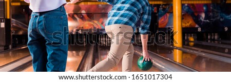 cropped view of girl standing near man throwing bowling ball on skittle alley, panoramic shot