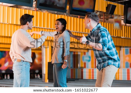 cheerful african american girl pointing with finger near happy multicultural friends in bowling club