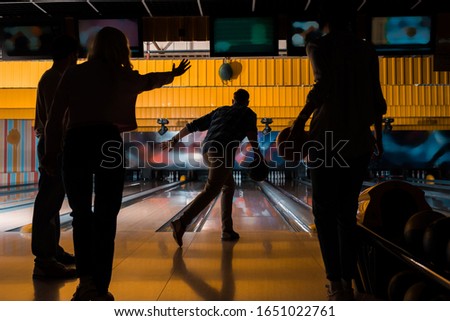 dark silhouettes of four friends playing bowling in bowling club