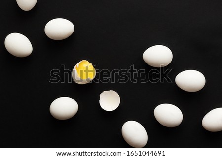 White eggs lie scattered on a black background. One egg is broken and the yolk is visible. Minimalistic design and color trend 2020. Top view