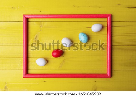 Painted Easter eggs in picture frame on yellow wooden background