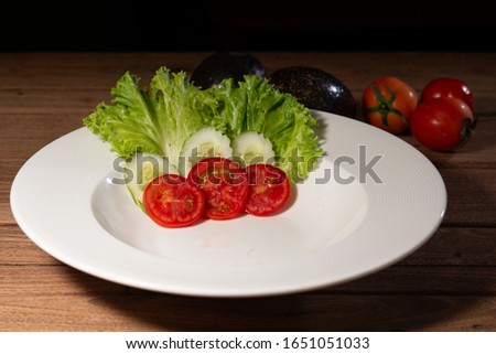 tomato slice, cucumber slice and salad in white circle dish with fresh tomato and avocado on wood table stock photo