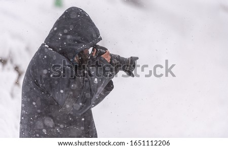 Female photographer holding camera taking images with snow falling in winter.
