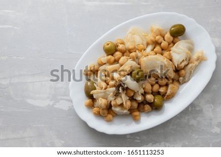 cod fish with chick pea and olives on white dish on ceramic background