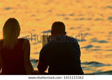 a couple on the seafront are viewing photos on a mobile phone