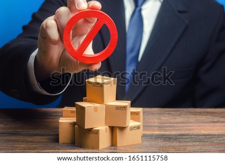 Businessman man official holding red prohibition sign NO over boxes with goods. Out of stock. Embargo trade wars. Restriction import, ban export of dual use goods to countries under sanctions.