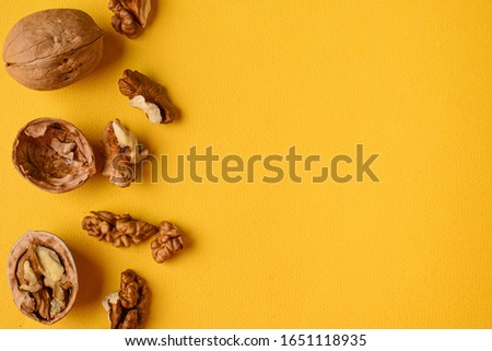  whole and uncovered walnuts  on a bright yellow plain background, space for text Royalty-Free Stock Photo #1651118935