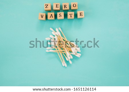 Eco-friendly biodegradable compostable bamboo cotton swabs or cotton buds like alternative for plastic is seen on greeen-blue background with letters "zero waste" 