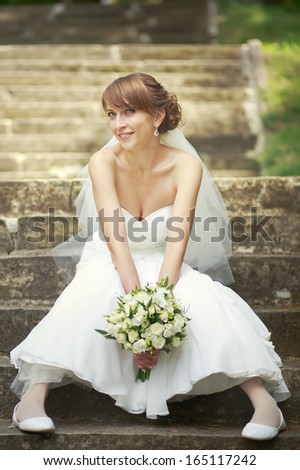 Happy young bride sitting on steps. Summertime picture.