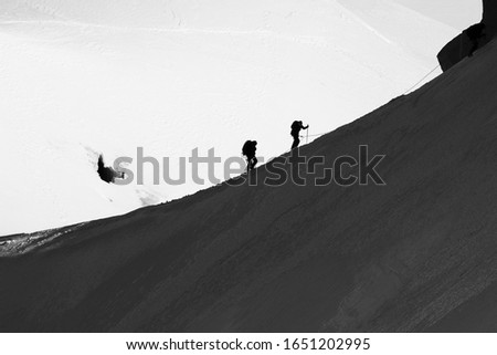 Silhouettes of two climbers hiking snowy Mont Blanc in the French Alps. Black and white photo.