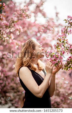 blonde girl in a black dress on a background of blooming pink sakura