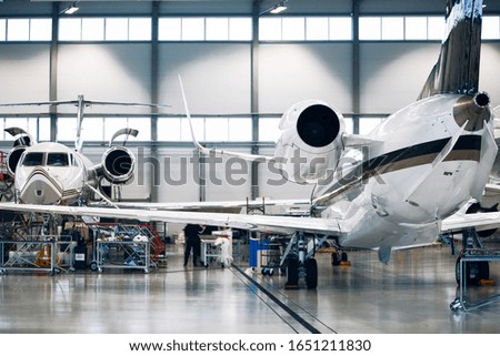 Maintenance of airplane in large white hangar Royalty-Free Stock Photo #1651211830