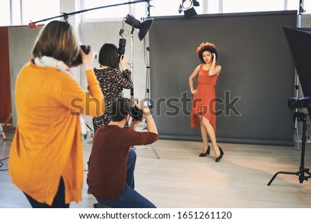Three attendees  standing in studio and taking photos of beautiful mixed race female model.
