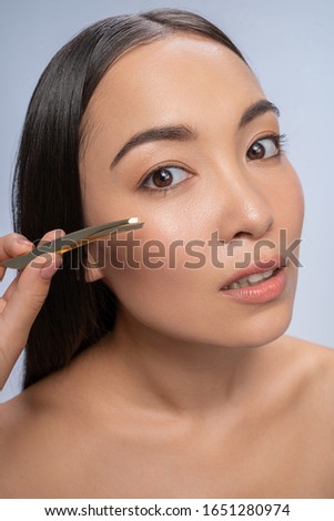 Young brunette woman using tweezers while doing beauty procedure