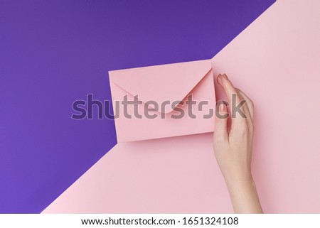 Pink envelope in woman's hand on the double colored pink and violet background. Mail concept
