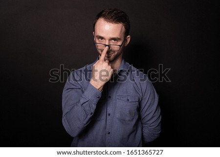 Attractive clever caucasian brunette man with dark eyes in casual shirt wearing glasses, playfully looking at camera. Self development training and education concept. Isolated on black background.