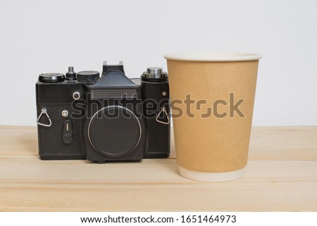 Mock up paper craft glass for coffee and vintage camera on wooden table and white background.