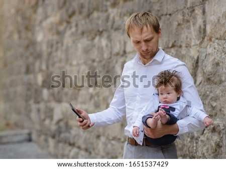 Business at home. Young father talking on mobile phone and nursing newborn child, copy space