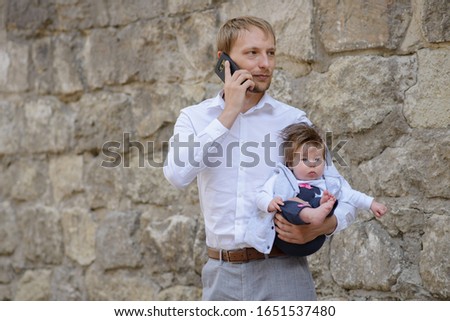 Business at home. Young father talking on mobile phone and nursing newborn child, copy space