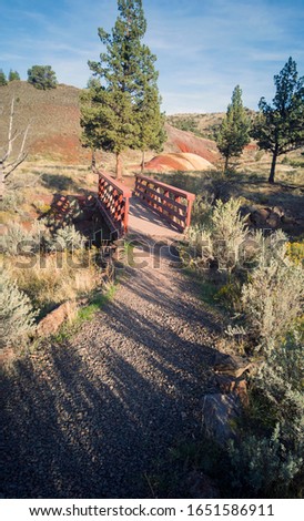 A bridge with red railings and a red and yellow mound in the background 
 in park called the John Day Fossil Beds on the Red Hill Trail in Mitchell Oregon