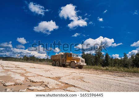 Industrial dusty road of clay quarry. A transport machine transports building materials. Summer sunny day with blue sky and white clouds. Heavy duty machinery activity.