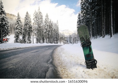 Snowboard in snow near road trace on beautiful snowy forest and mountains background in sunny day.