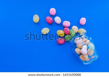 Group of Scattered Colorful candies on blue background with glass jar. Confectionery and sweets store concept. Stock photo.