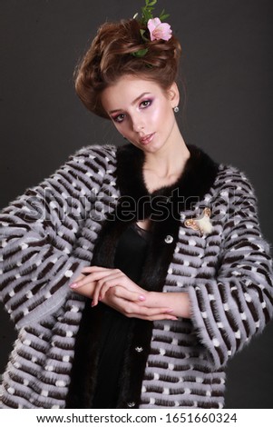 Close up portrait of beautiful fashion model in autumn / winter clothes furs posing on gray background. Wearing stylish fluffy coat. Hairstyle decorated with a flower