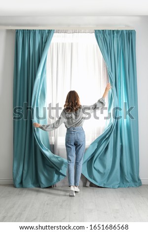 Woman opening window curtains at home in morning, back view Royalty-Free Stock Photo #1651686568