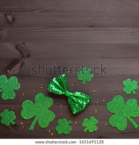 Happy Saint Patrick's Day greeting card with traditional symbols, shamrock, green attire. Green hat, bow tie, St Patricks Day shamrocks, golden confetti on dark wooden background, copy space