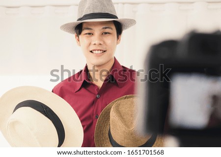 Happy young attractive Asian male blogger or vlogger present and review hat on live streaming broadcast with internet subscribers. Social media influence people, content maker, e-commerce concept.