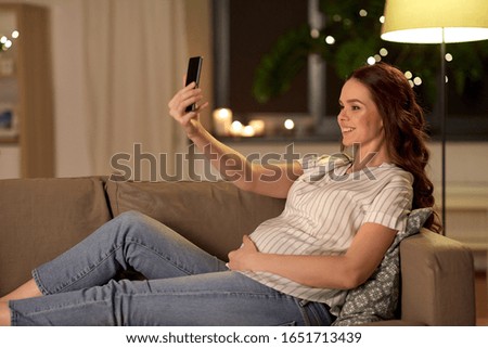 pregnancy, technology and people concept - happy smiling pregnant woman taking selfie with smartphone on sofa at home