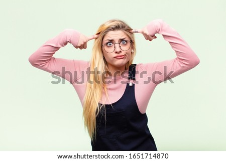 young pretty blonde woman with a serious and concentrated look, brainstorming and thinking about a challenging problem against flat wall