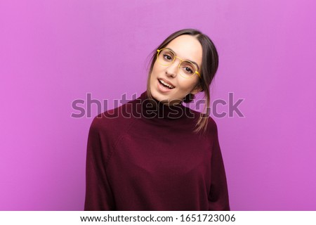 young pretty woman with a big, friendly, carefree smile, looking positive, relaxed and happy, chilling against purple wall